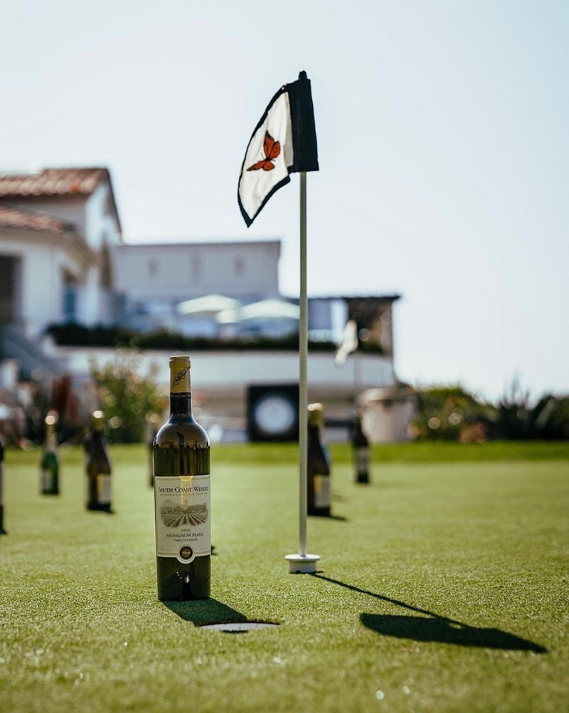 Wine bottles displayed beside a flag on a putting green at a brand experience