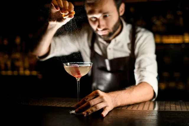 A bartender finishing a cocktail behind a bar