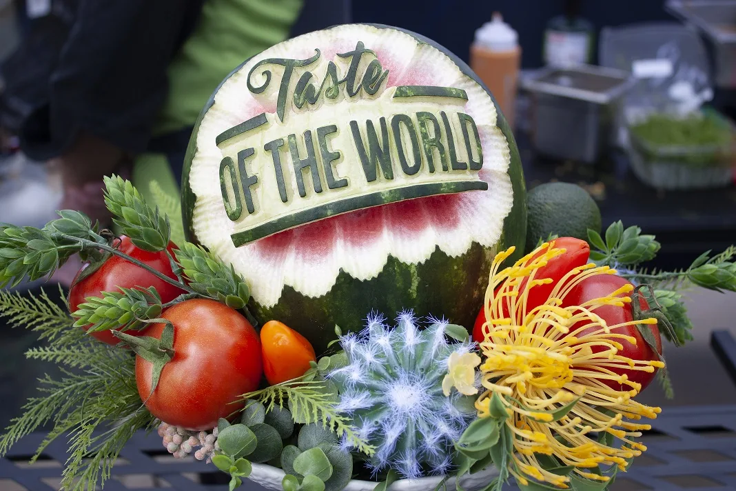 Carved watermelon with the Taste of the World name surrounded by a colorful culinary display