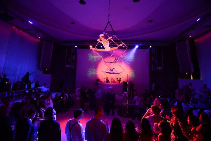 Guests at a live event with aerial performers and violet stage lighting